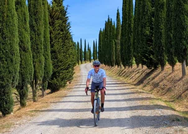 Cyclist gravel riding in Tuscany along a gavel road linted with cypress trees