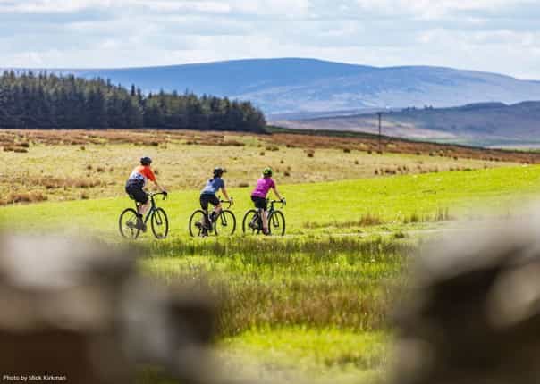 Cyclists gravel riding through green hills of Northumberland on a cycling tour