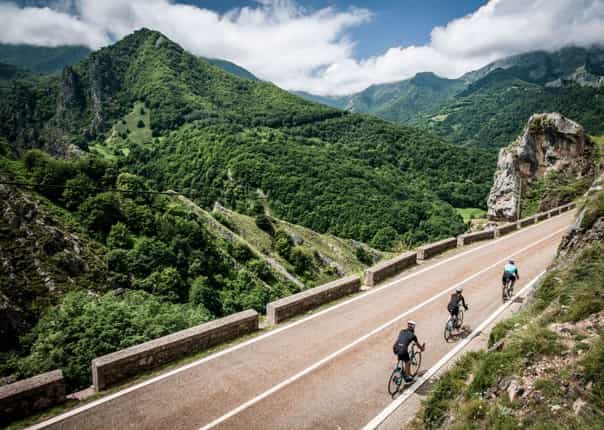 Three road cyclists riding a scenic mountain road in Northern Spain