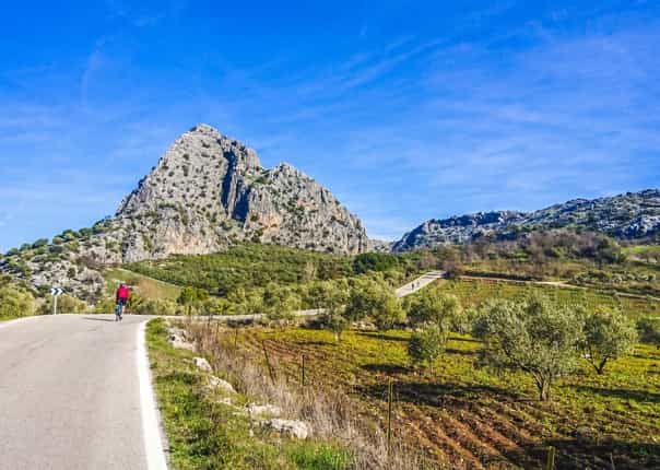 Cyclist riding towards limestone peak in the Sierra de Grazalema Natural Park in Andalucia