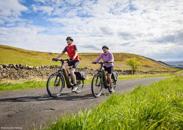 Two happy cyclists riding electric bikes on the Hadrian's Cycleway route through Northumberland