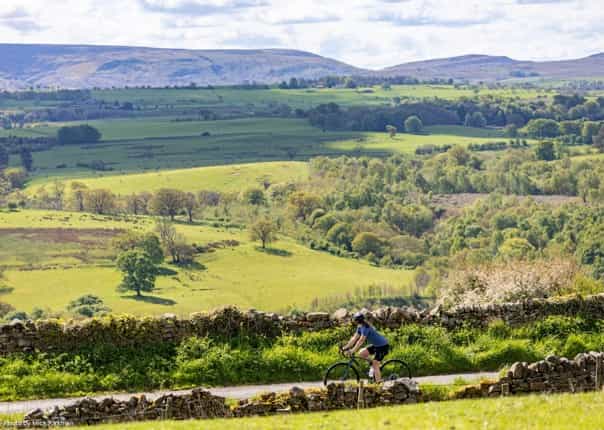 Road cyclist riding through rolling green hills of England on LEJOG cycle route