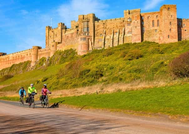 Cyclists riding past Bamburgh Castle on the Coast and Castles cycling holiday.png