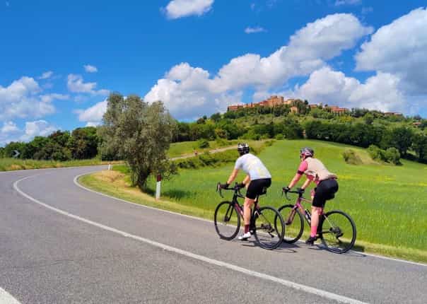 Two road cyclists ascending through rolling green hills of Tuscany on a guided cycling tour