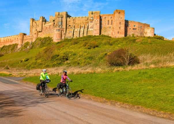 Cyclists riding past Bamburgh Castle