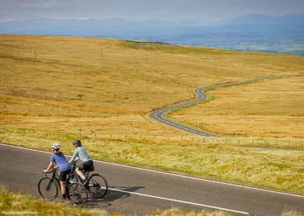Two cyclists riding the winding road of Hartside in Northern England on the coast to coast C2C route.png