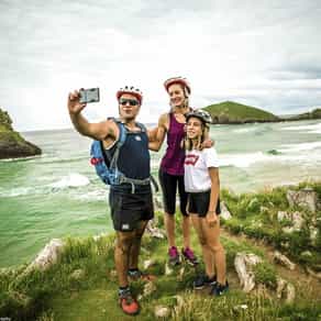 A family of three cyclists taking a selfie overlooking the ocean in Spain on a cycling holiday